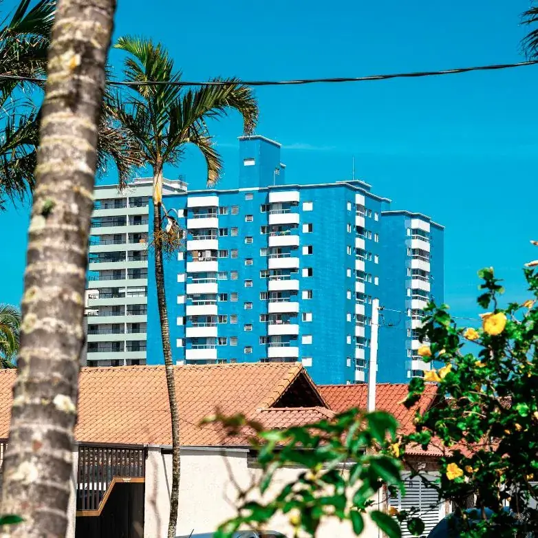 A blue condominium tower behind palm trees and a tiled roof