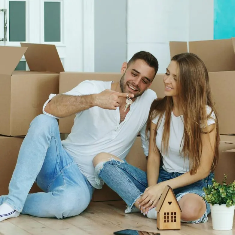 A couple sitting among moving boxes in their new home, holding the keys